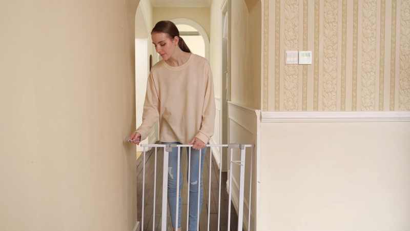 A Woman Is Locking a White Dog Barrier Gate in A Hallway, Ensuring a Secure Separation Between Spaces