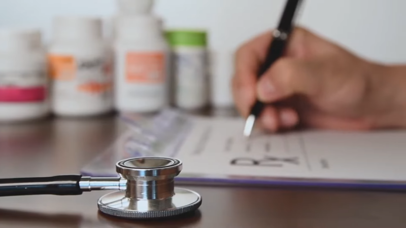 A Stethoscope on A Desk Next to Bottles of Medication While a Person Writes a Prescription for Heart Disease in Dogs